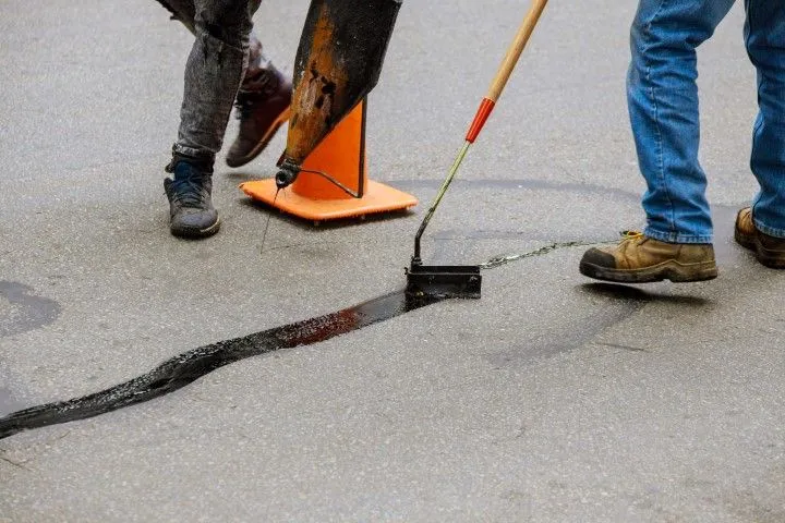 Two people repairing asphalt crack with sealant, one using a roller. Orange cone visible in Benton, Arkansas