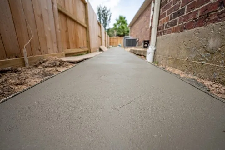 Newly poured concrete pathway between a wooden fence and a brick building in Benton, Arkansas
